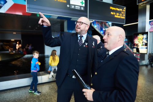 Mannelijke beveiliger in uniform praat met een mannelijke collega en wijst naar boven.