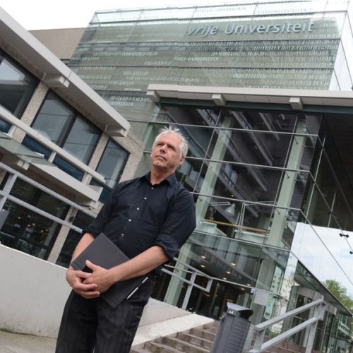 Man staat voor de Vrije Universiteit van Amsterdam met map in zijn hand.