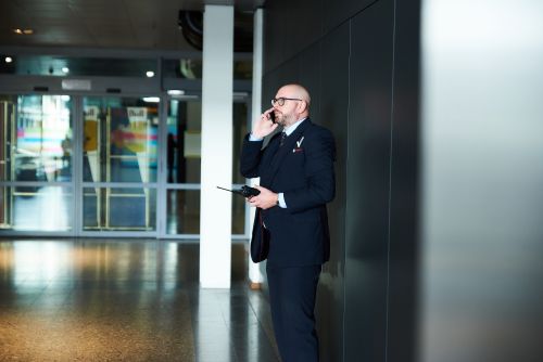 Mannelijke beveiliger loopt in uniform rond en praat in een telefoon.