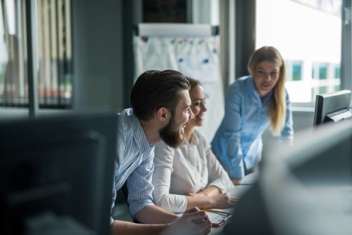 drie projectmanagers met elkaar in gesprek aan bureau kijkend naar beeldscherm.