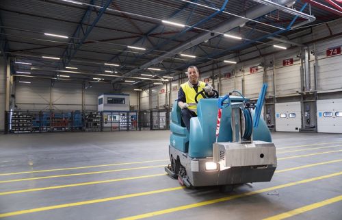 Een schoonmaakmedewerker van Gom Logistiek zit op een schrobzuigmachine en maakt de vloer in een distributiehal schoon