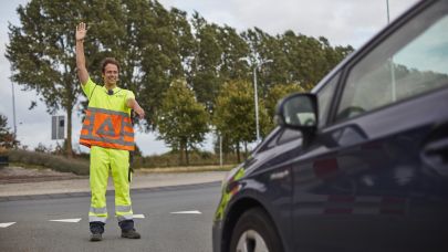 Verkeersregelaar in oranje en geel uniform steekt zijn hand omhoog en houdt een auto tegen.