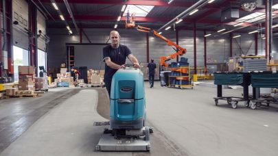 een medewerker van Gom Logistiek loopt achter een schrobzuigmachine en maakt hiermee de vloer van een distributiecentrum schoon