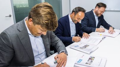 3 personen zitten aan tafel en tekenen een contract