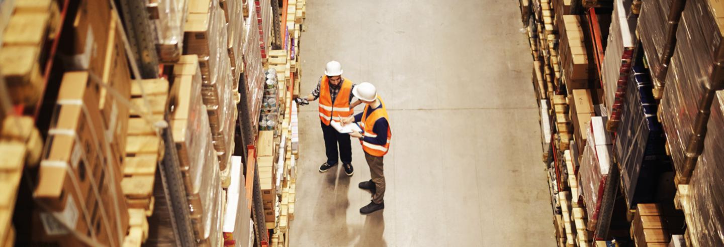 Een groot magazijn met voorraad op enorme schappen met daarnaast twee medewerkers die in gesprek zijn met elkaar