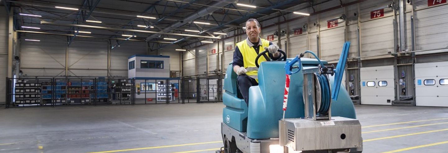 Een schoonmaakmedewerker van Gom Logistiek zit op een schrobzuigmachine en maakt de vloer in een distributiehal schoon