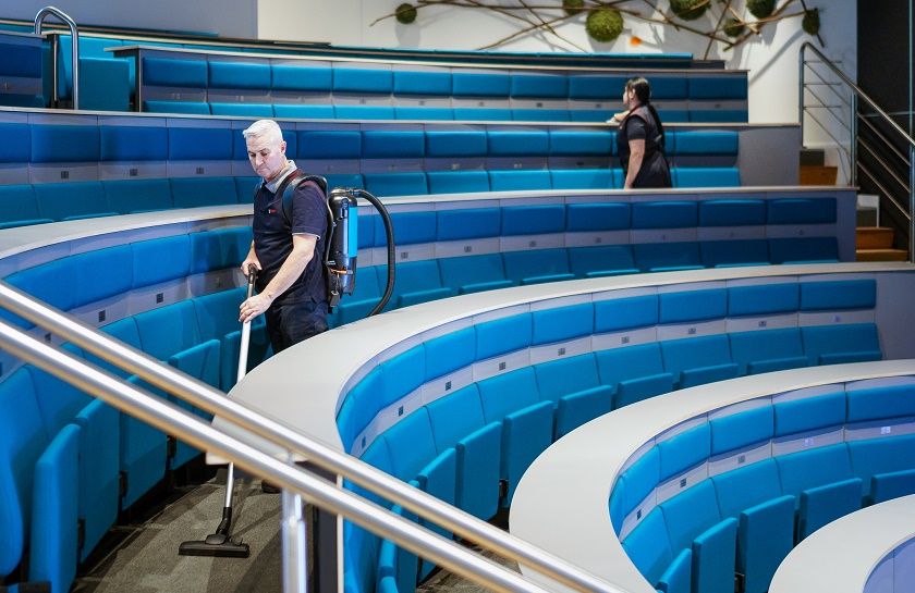 2 medewerkers van Gom Onderwijs maken het auditorium schoon, de een stofzuigt de ander maakt de stoelen schoon